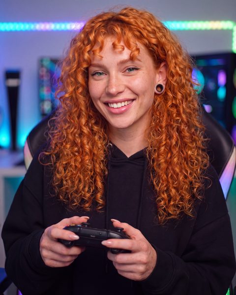 Freya in a black hoodie holding a game controller in front of a neon-lit gaming setup.